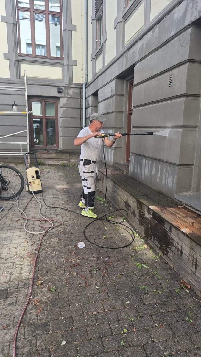 Maler som spyler ned en pusset fasade med høytrykk før arbeidet starter